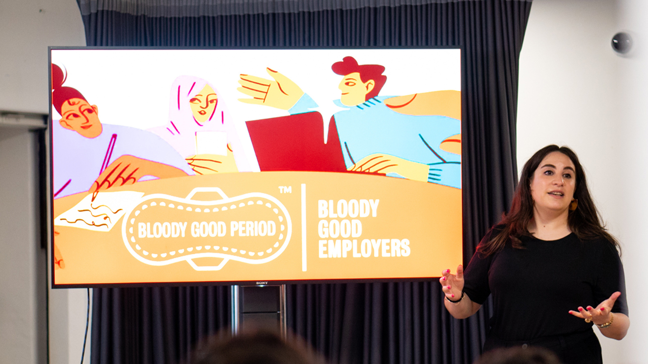A Bloody Good Period slide shown on a TV with the female speaker presenting next to the screen