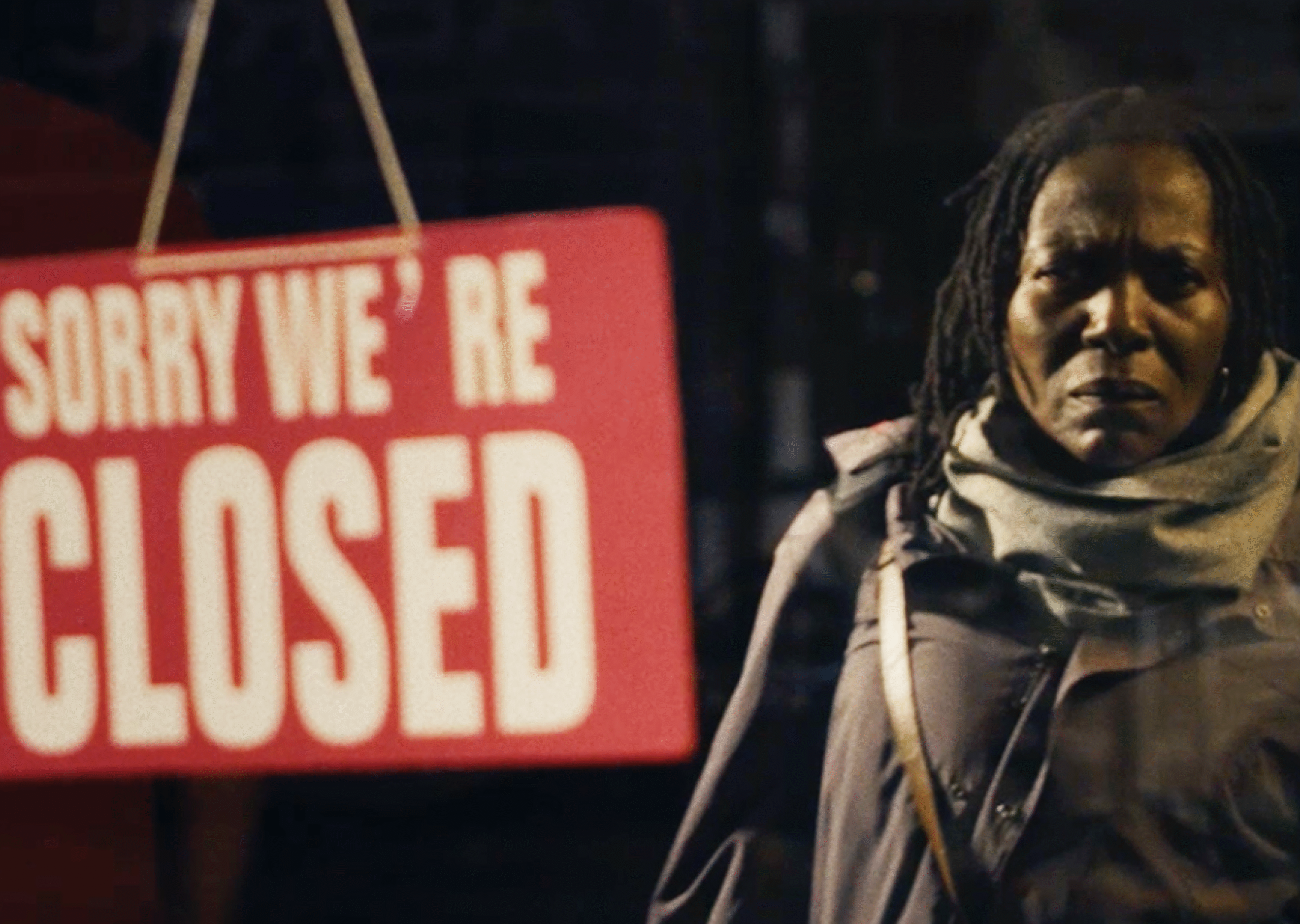 A still from the First Day campaign film for Crisis of a reflection of Michelle in a glass door with a 'Sorry we're closed' red sign.