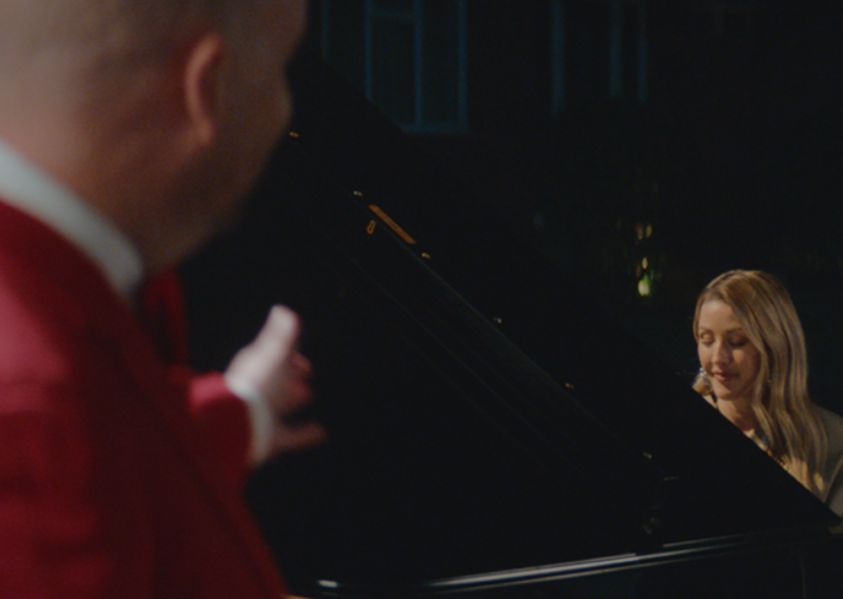 A standing man points towards Ellie Goulding who is playing the piano and singing